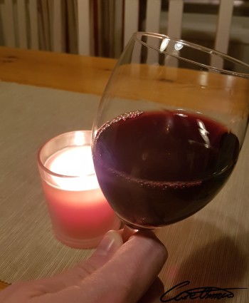 An hand holding a glas of red wine with a candle in the background
