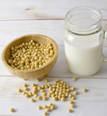 Care Omnia Glass of soy milk next to a bowl of soy beans