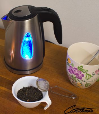 A water cooker, a big cup and some tea on a wooden surface