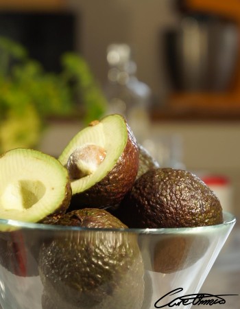 Glass bowl with some avocados. One is cut in half.