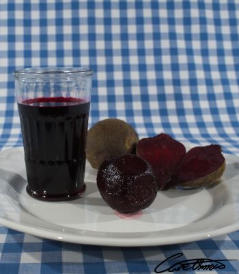 A glass off beetroot juice, a cooked beetroot and a raw beetroot cut in half