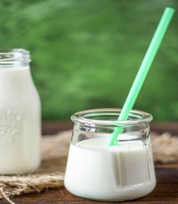 A bottle of milk. A glass of milk with a green straw.