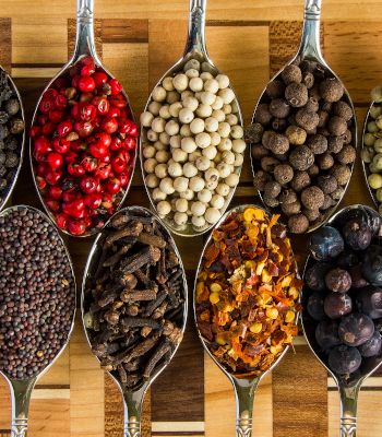 Spoons on a wooden table filled with different spices