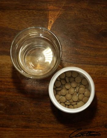 A glass of water and iron supplement tablets in a can on a wooden surface