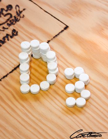 Tablets of Vitamin D supplements on a wooden surface arranged to form the letter D and the number 3